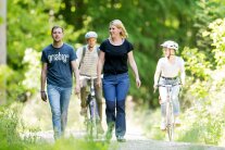 Zwei Spaziergänger gehen auf einem Waldweg spazieren, zwei Radfahrer holen von hinten auf