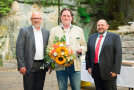 Der Herren posieren für die Kamera. Der Mann in der Mitte hat enen Blumenstrauß in der Hand