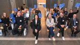 Ministerin Kaniber sitzt mit den Absolventen auf Stühlen während diese Ihre Zertifikate in die Kamera halten