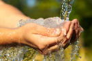 Zwei Hände unter einem dicken Wasserstrahl.