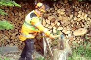 Mann in Schutzkleidung spaltet Holz auf einem Hackstock