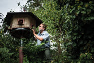 Ein Mann kniet neben einem Luxusvogelfutterhaus