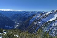 Blick von einer Anhöhe in ein Gebirgstal im Winter bei wolkenlosem Himmel