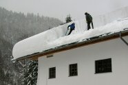 Zwei Leute stehen auf einem Dach und schippen den meterhohen Schnee runter