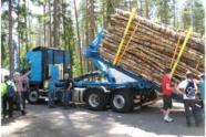Ein LKW nimmt einen mit Holz beladenen Rungenkorb mit Hilfe des Containerlifthakens auf.