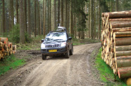 Auto mit Aufbau auf dem Dach passiert einen Holzpolter auf einem Waldweg.