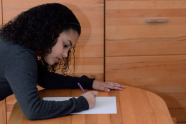 Mädchen sitzt an einem Holzschreibtisch vor einem Holzschrank