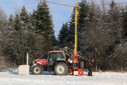 Traktor mit Seilkran im Winter auf einem Feld vor einem Bestand