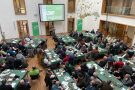 Tagungsteilnehmer an Tischen vor einer großen Leinwand
