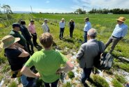 Eine Gruppe Menschen steht auf einer landwirtschaftlichen Fläche im Kreis