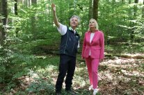 Mann und Frau stehen im Wald, der Mann zeigt in das Kronendach
