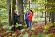 Försterin berät Waldbesitzerpaar. Sie stehen vor einer als Biotopbaum markierten Buche.