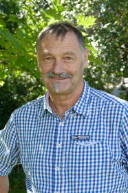 Portrait eines Herren mir grauen Haaren und Schnurbart in einem blau karierten Hemd