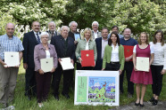 Frauen und Männer stehen mit Urkunden in der Hand vor einem Wald.