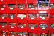 Regal mit roten Plastikboxen, in denen in Platsik verpacktes Saatgut lagert.