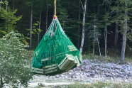 In einem Netz sind viele kleine Holzkisten; das Netz ist mit einem Seil an dem Helikopter befestigt.