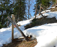 Das Bild zeigt einen beschneiten Hang und darauf befindliche Dreieckskonstruktionen aus jeweils drei Rundhölzern. 