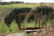 Holzrahmen und Bank auf einem Berg vor einem bewaldetem Tal.