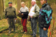 Drei ältere Herren stehen mit junger Försterin in einem Wald.