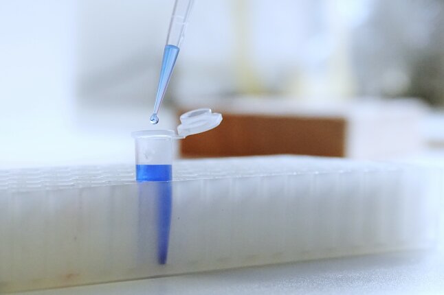 Laborröhrchen mit blauer Flüssigkeit und einer darüber hängenden Pipette mit Tropfen.