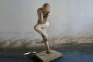 Skulptur einer nackten Frau, die auf einem Bein steht und sich die Ohren zu hält