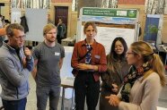 An einem Messestand informieren verschiedene Projektmitarbeitende interessierte Besucher.