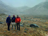 3 Wildbiologen auf einem in Nebel und etwas Schnee verhangenen Berg