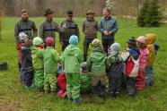 Eine Gruppe Menschen bestehend aus Männern mit Forstbehördenkleidung und Kindergartenkindern