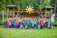 Die Teilnehmer der Kongresses stehen vor einer Tribüne aus Holz und gucken begeistert in die Kamera