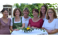 Sechs Frauen stehen um einen Tisch und lächeln in die Kamera