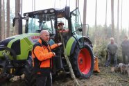 Mann mit oranger Warnjacke steckt vor einem Forstschlepper, in dem anderer Mann von einem Baumstamm eingeklemmt sitzt