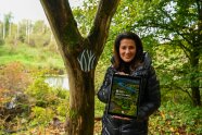 Die Forstministerin steht vor einem Baum und zeigt mit einem Tablet die App