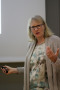 Blonde Frau in brauner Jacke und Brille hält einen Powerpoint-Vortrag