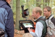 Mehrere Herren stehen mit Spezialgeräten in einem Laubwald.