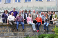 Gruppenbild: Einige Personen sitzen auf einer Mauer, weitere stehen an einem Geländer dahinter.