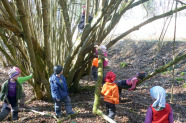 Einige Kinder spielen neben einem Baum im Wald.