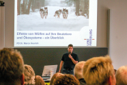 Ein Mann steht in einem Hörsaal vor Publikum und präsentiert Wölfe