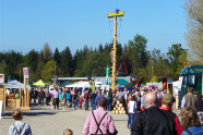 Viele Menschen stehen auf einem Ausstellungsplatz und unterhalten sich. Kinder klettern einen Kletterbaum hinauf.