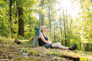 Eine Frau lehnt in einem lichten Wald an einen Baumstumpf